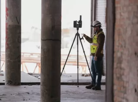 Мужчина в средствах индивидуальной защиты внутри заброшенного здания, наземное лазерное сканирование с фокусом FARO на штативе