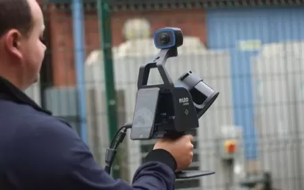 Мужчина держит сканер FARO Orbis Mobile LiDAR, в средствах индивидуальной защиты на открытом воздухе