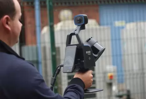 Мужчина держит сканер FARO Orbis Mobile LiDAR, в средствах индивидуальной защиты на открытом воздухе